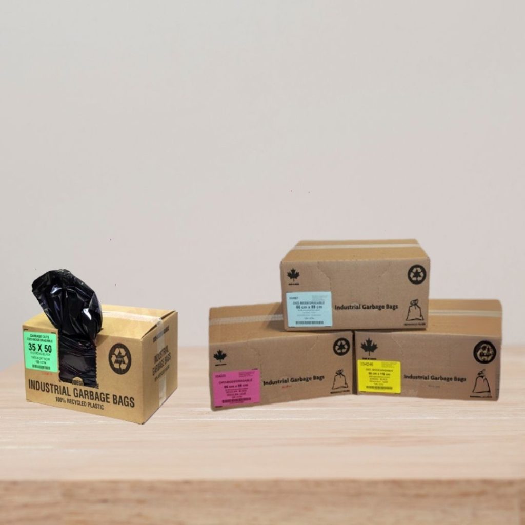 Cardboard dispenser boxes of industrial garbage bags manufactured by a top North American plastic bag manufacturer, featuring an open box dispensing a heavy-duty black trash bag alongside stacked cases with color-coded labels.