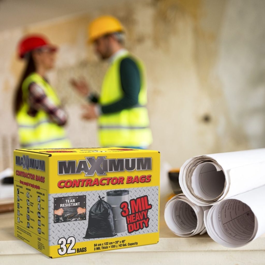 A yellow box of Maximum Contractor 3 Mil heavy-duty bags sits next to rolled-up construction blueprints, with two construction workers in high-visibility vests conversing in a blurred background.